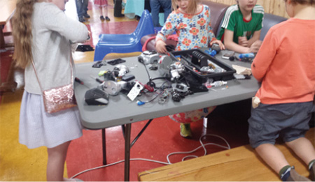 Kids around a table building with electronic parts.