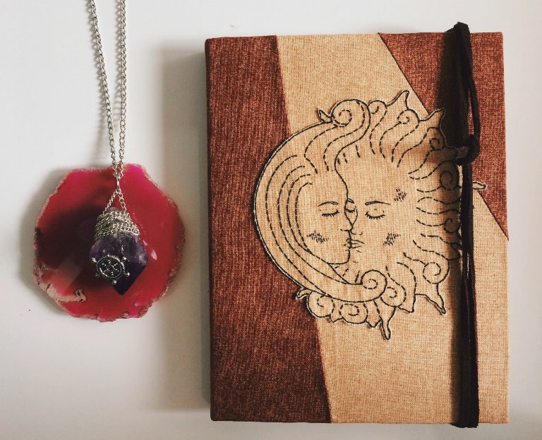 Photograph of a book with an entwined sun and moon on the cover. The image on the book has been made out of textiles and sewn together.