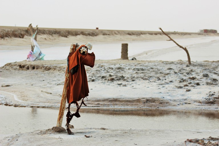 A desert landscape with dead trees. Some clothing hangs fron a tree creating a humanoid figure