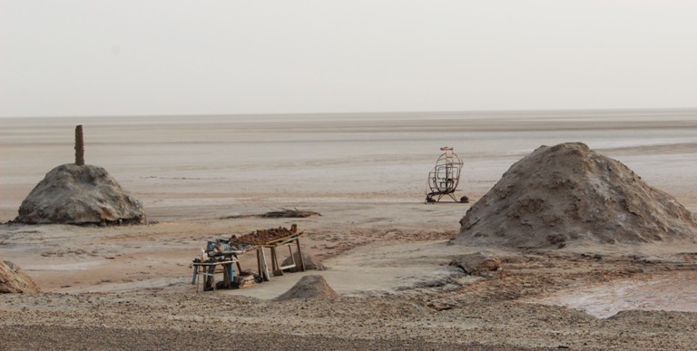 A desert landscape with two hillocks of dirt, A junk coverered table in the foreground and a wireframe sculpture in the background